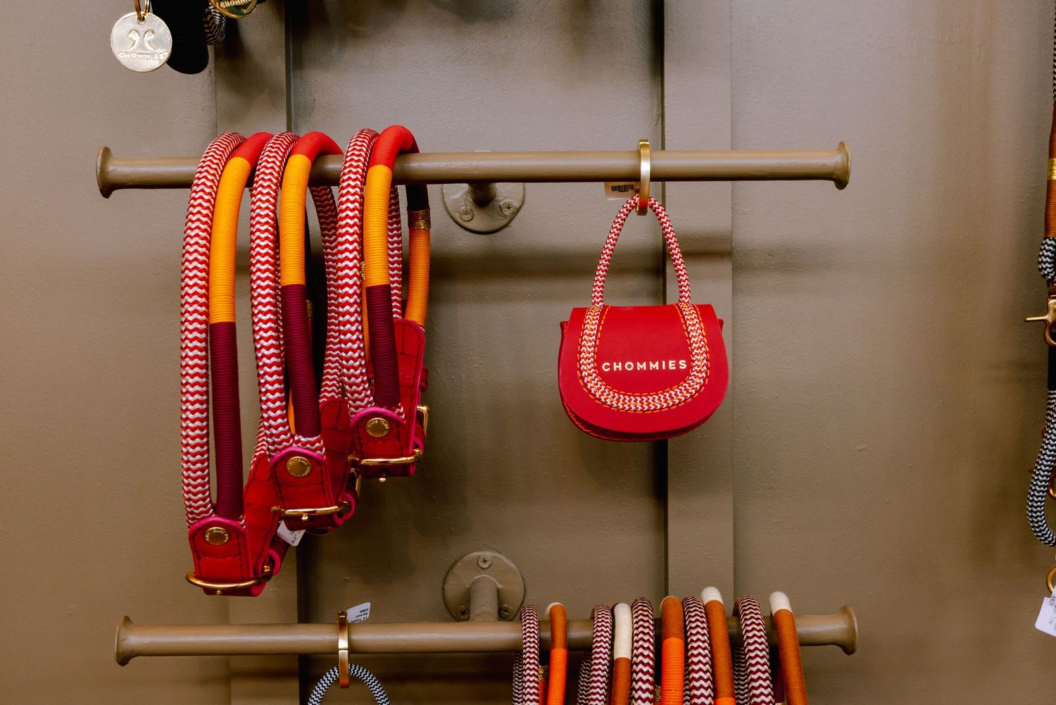 Red and orange dog leashes and accessories displayed on metal wall rack.