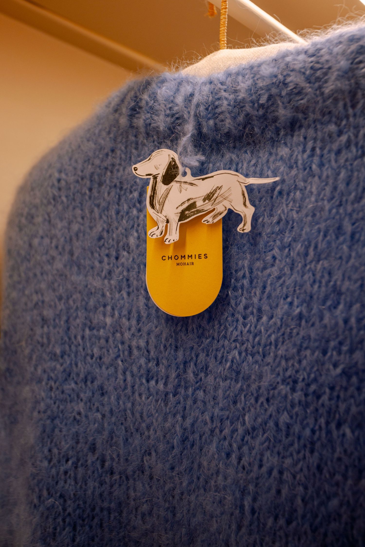 Silver dog pin attached to a blue knit sweater with yellow tag.