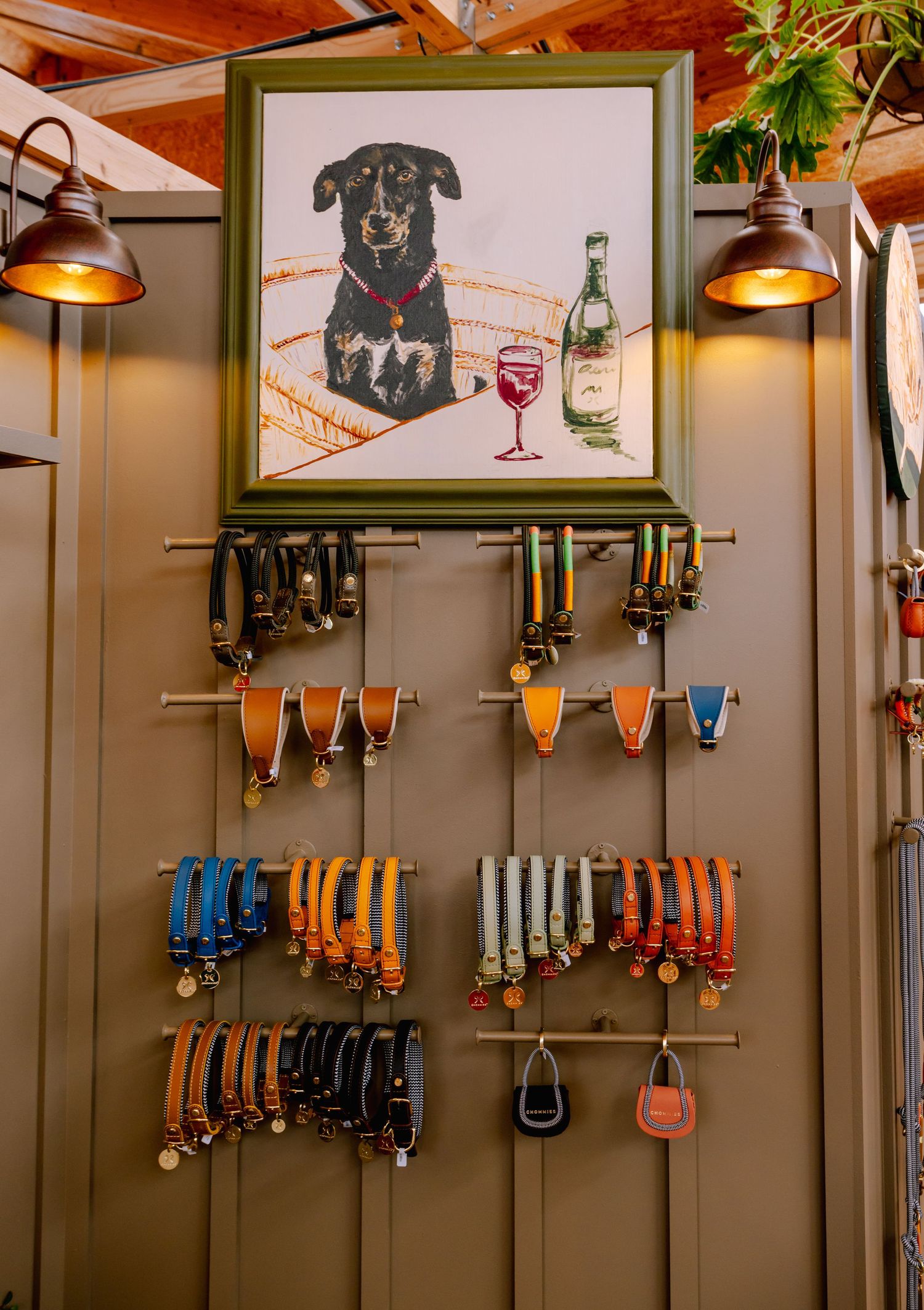 Wall display of colorful dog leashes beneath framed artwork of black dog with wine.