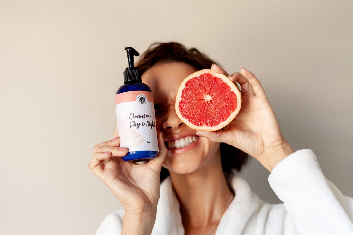 Person holding grapefruit and skincare product against white background.