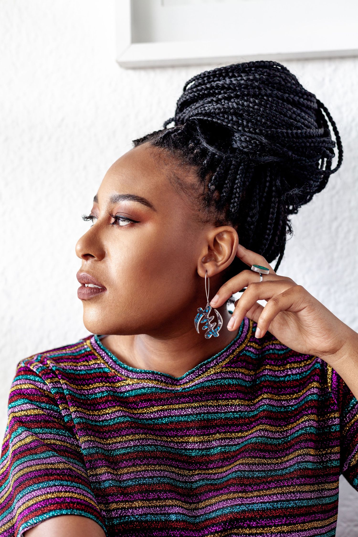 Portrait showing braided hairstyle and colorful striped sweater with statement earrings.