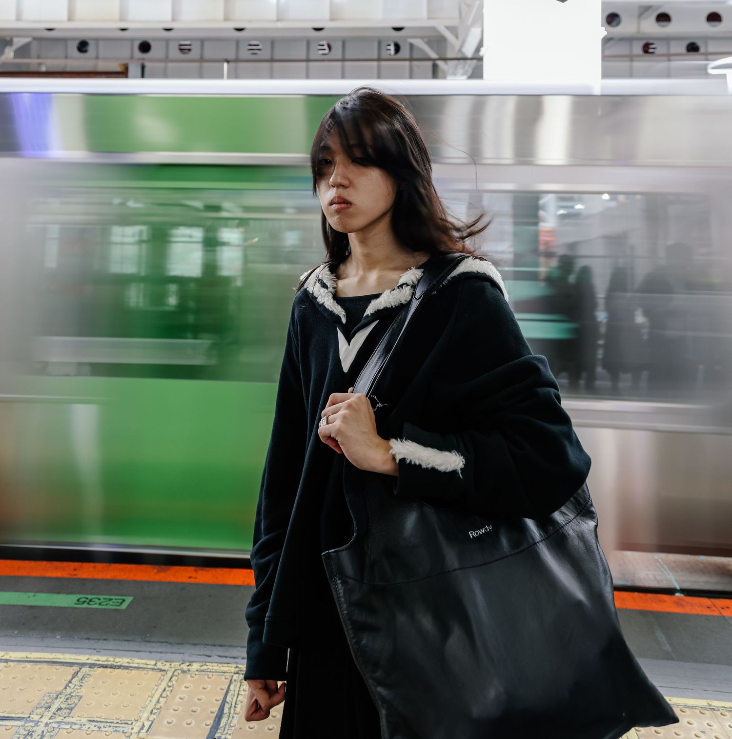 Person in black coat walking past a blurred green train in a subway station.