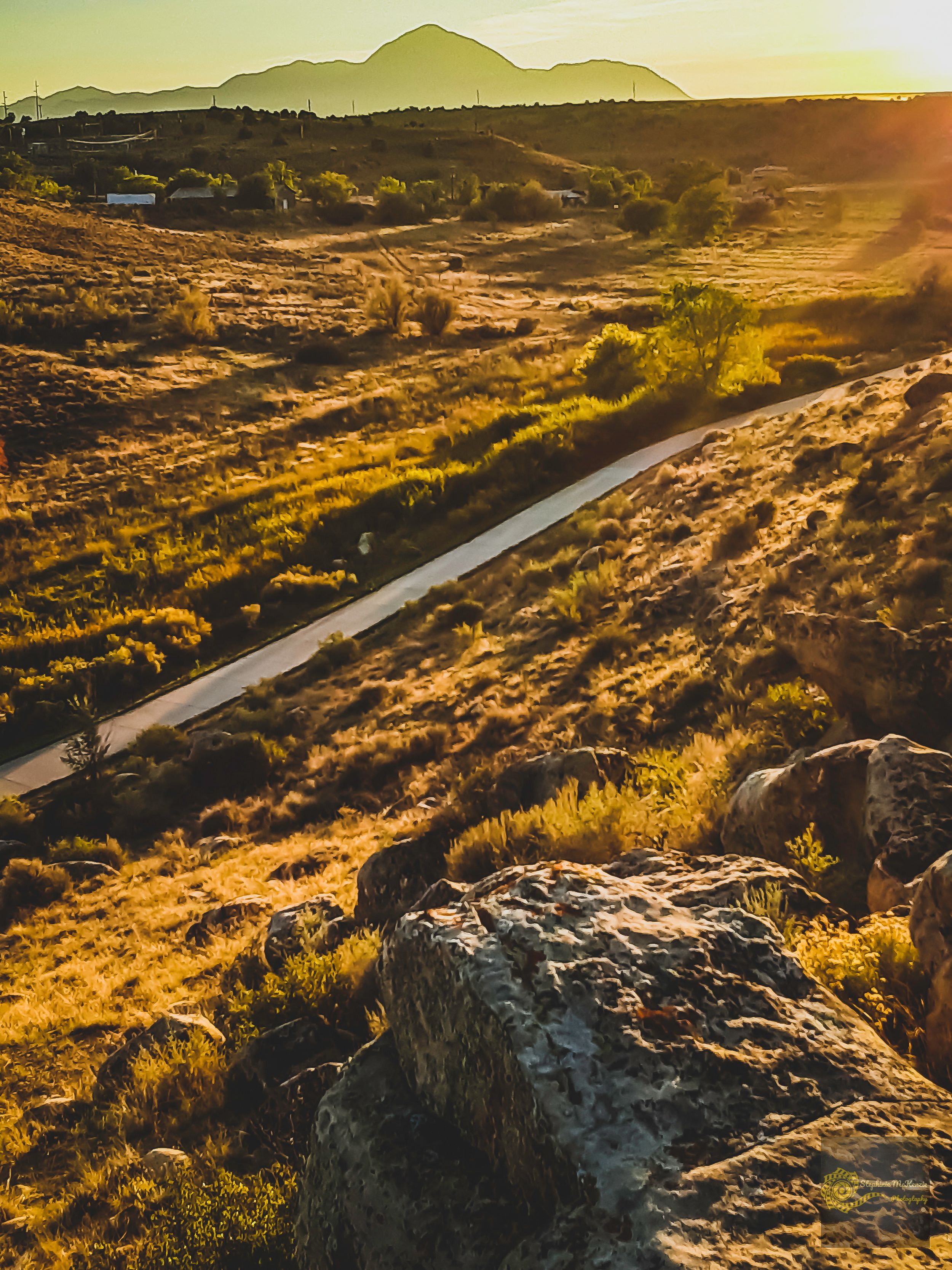 Golden sunset over desert landscape with winding road and mountain silhouette at golden hour.