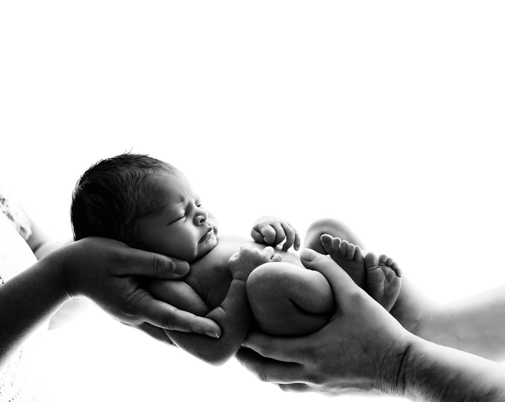 A tiny sleeping newborn baby cradled gently in adult hands in black and white photography.