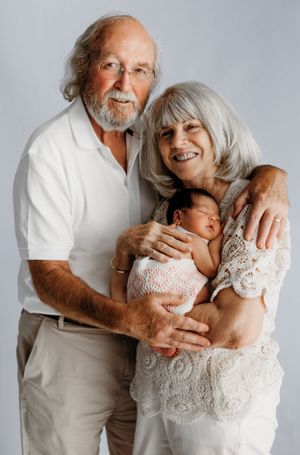 Portrait of grandparents holding a sleeping newborn baby against a white background.