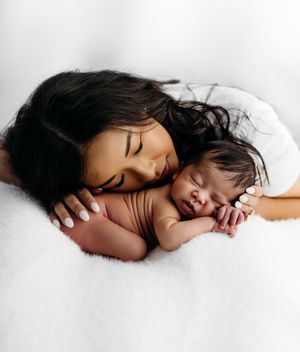 Mother and baby sleeping peacefully together on soft white bedding in tender embrace.