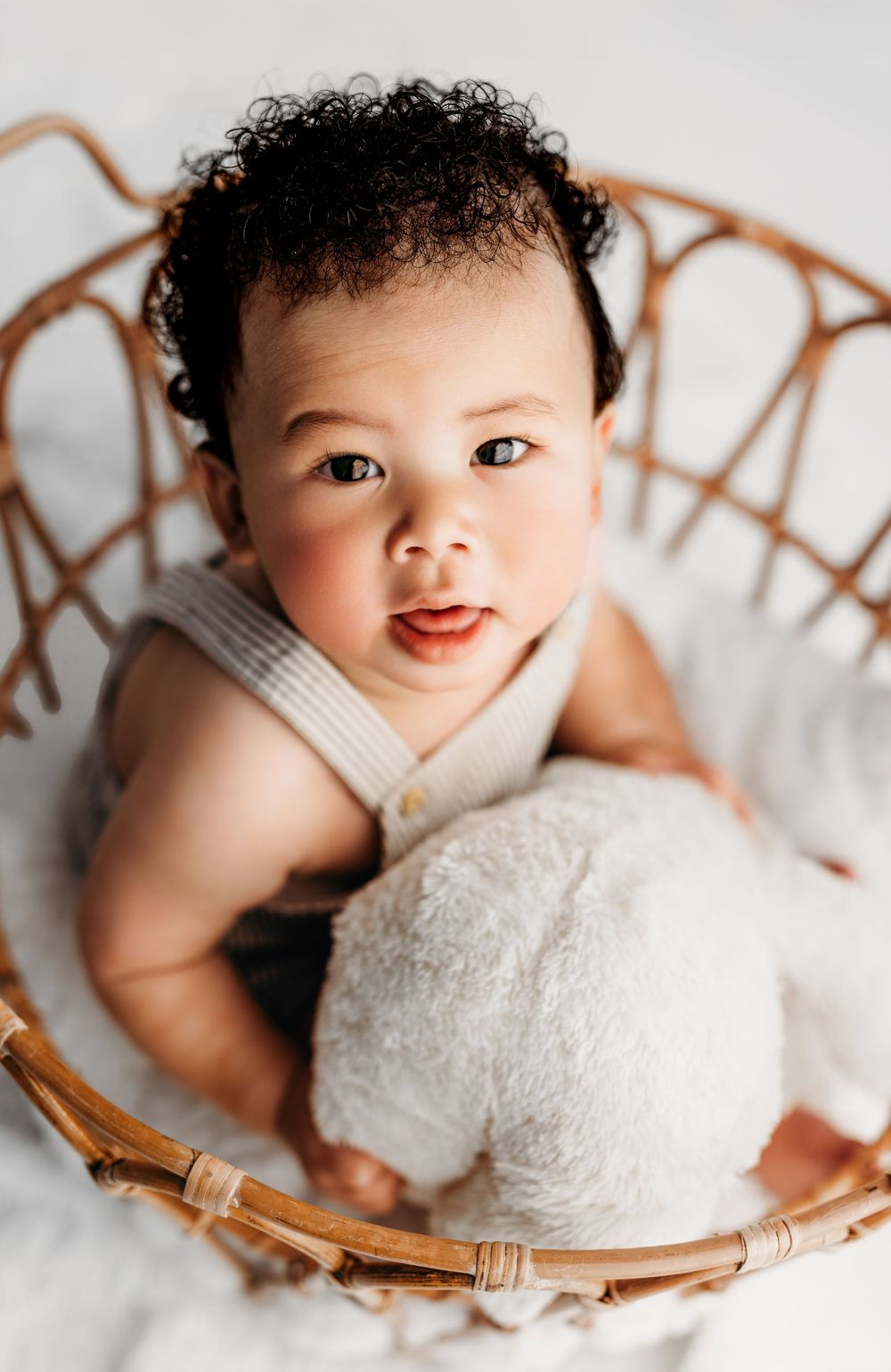Close-up images of cheerful baby with curly hair lying in white blankets and wicker baskets in studio setting.