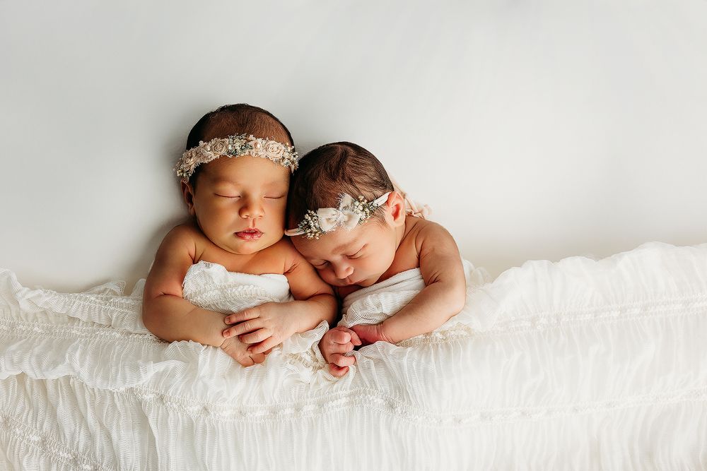 Sleeping newborn babies lie together on soft white blankets in a series of tender professional portraits.