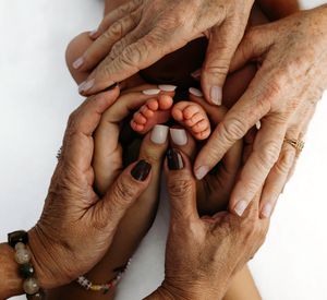 Adult hands gently hold tiny newborn baby feet against white background, showing tender generational touch.