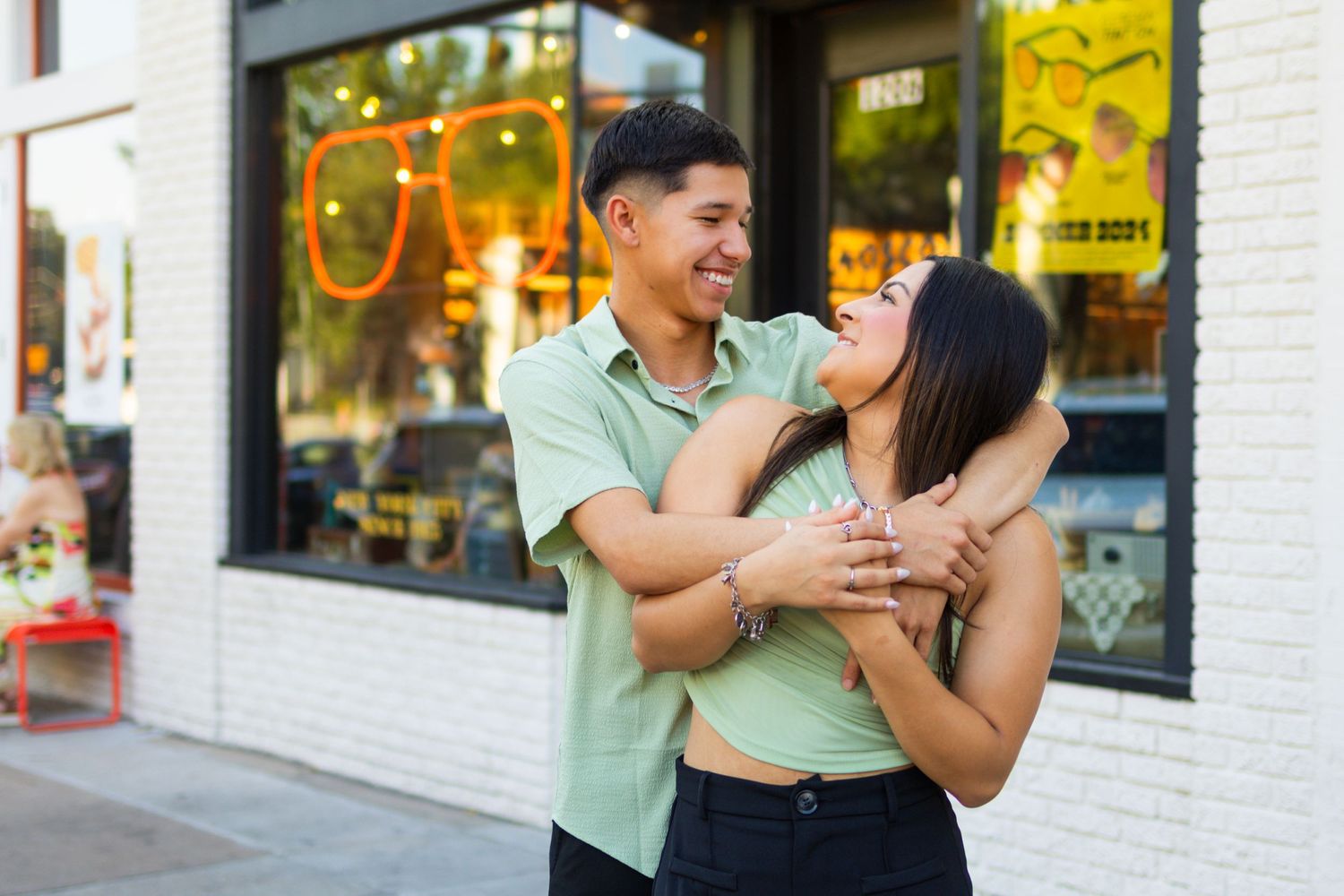 A playful urban couple shoot with storefront windows and city lights in the background.