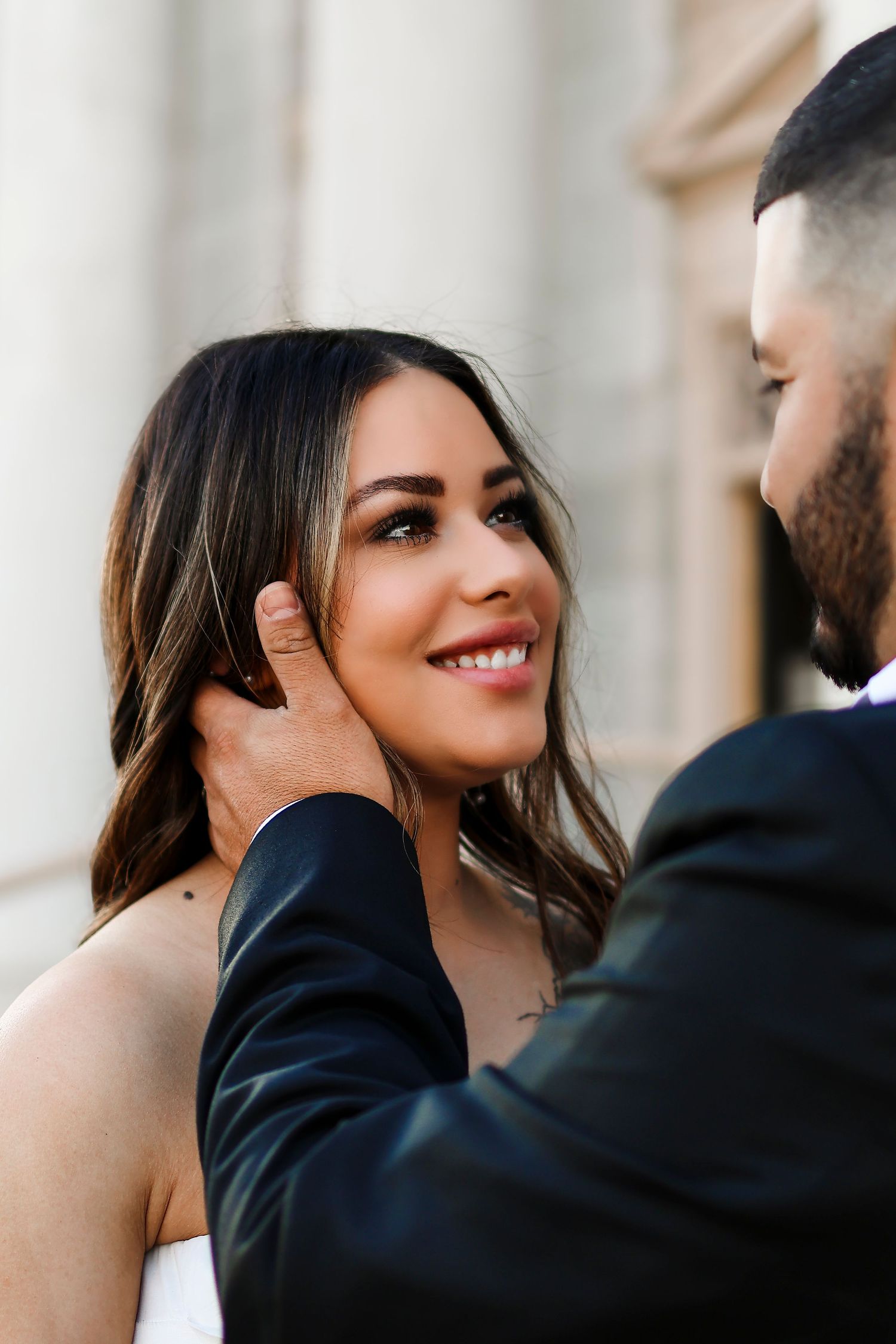 Romantic engagement photo of a couple sharing an intimate moment against white columns.