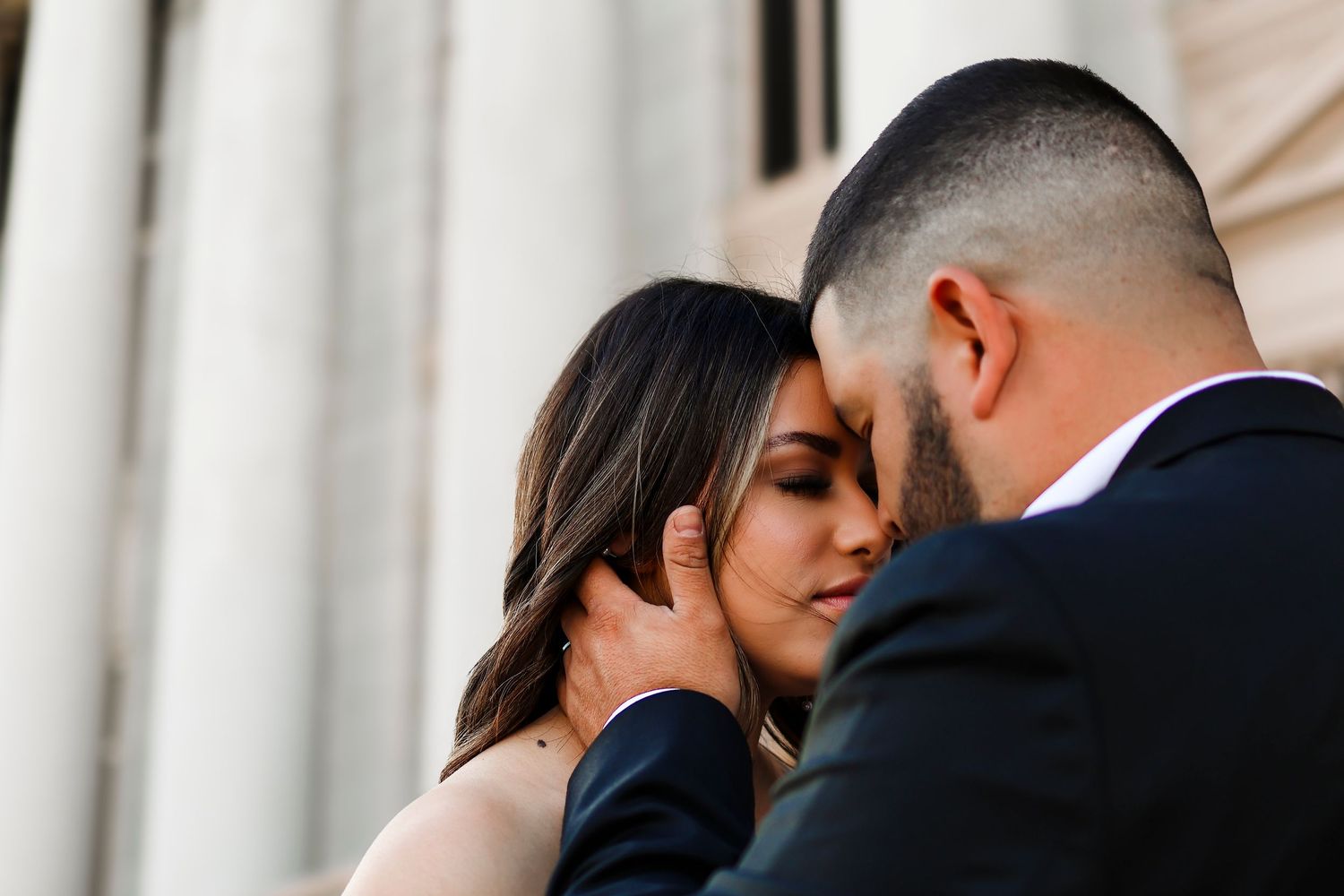 Couple sharing a tender moment during their wedding photoshoot near classical architecture.