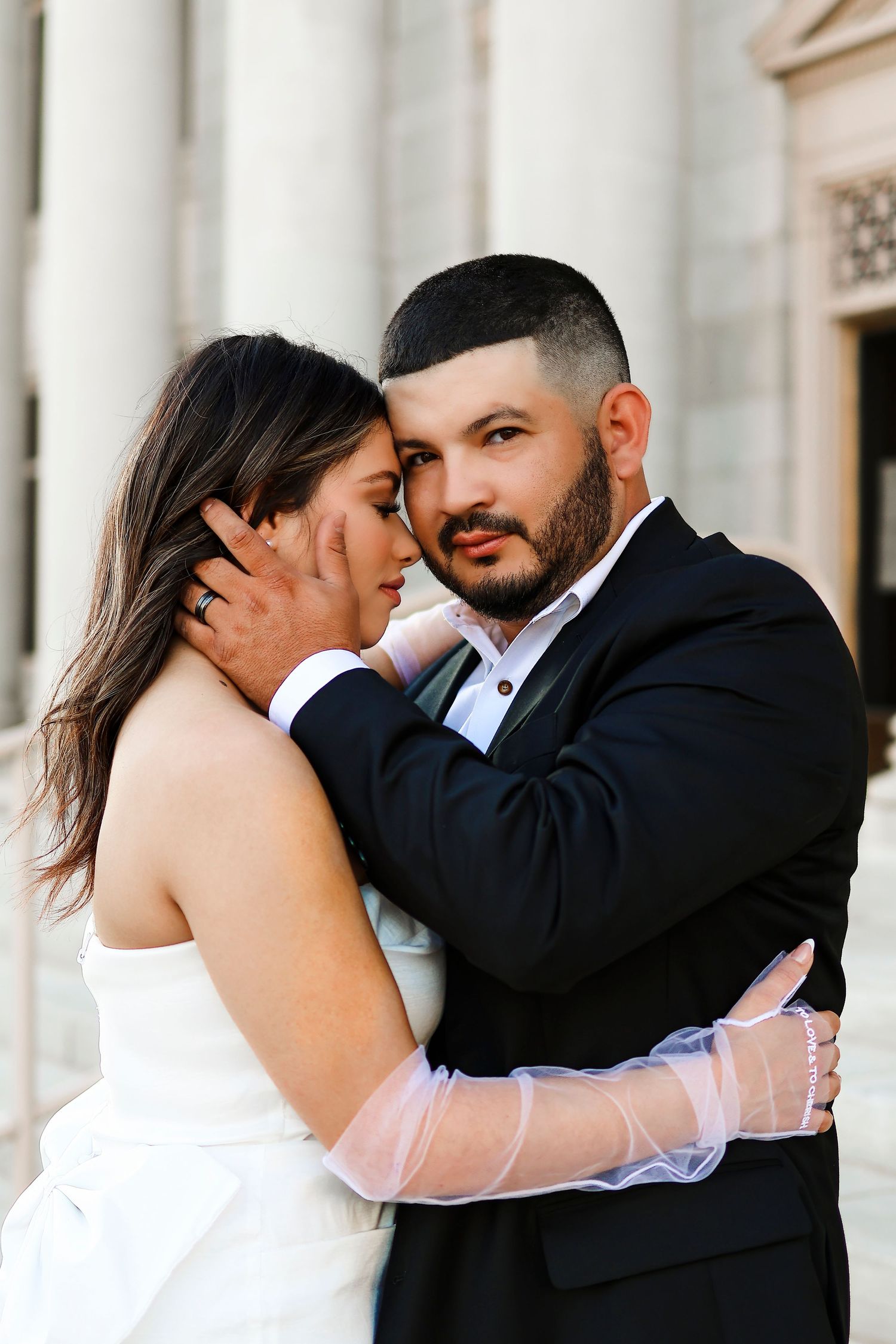 Intimate wedding portrait of newlyweds embracing against classic white columns.
