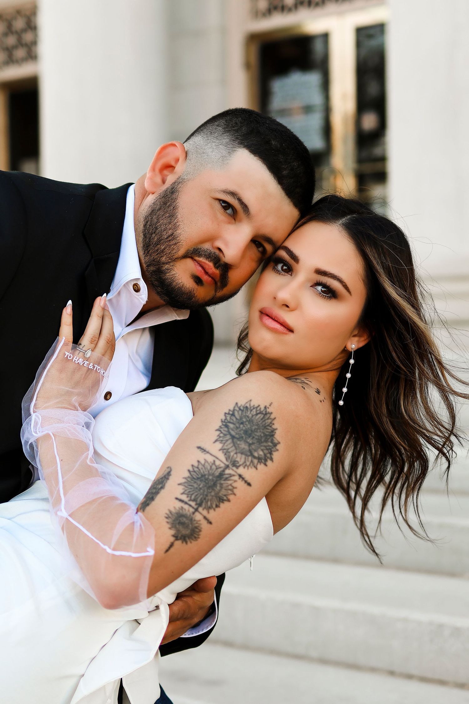 Stylish wedding couple pose together showing bride's floral tattoo and sheer sleeve details.