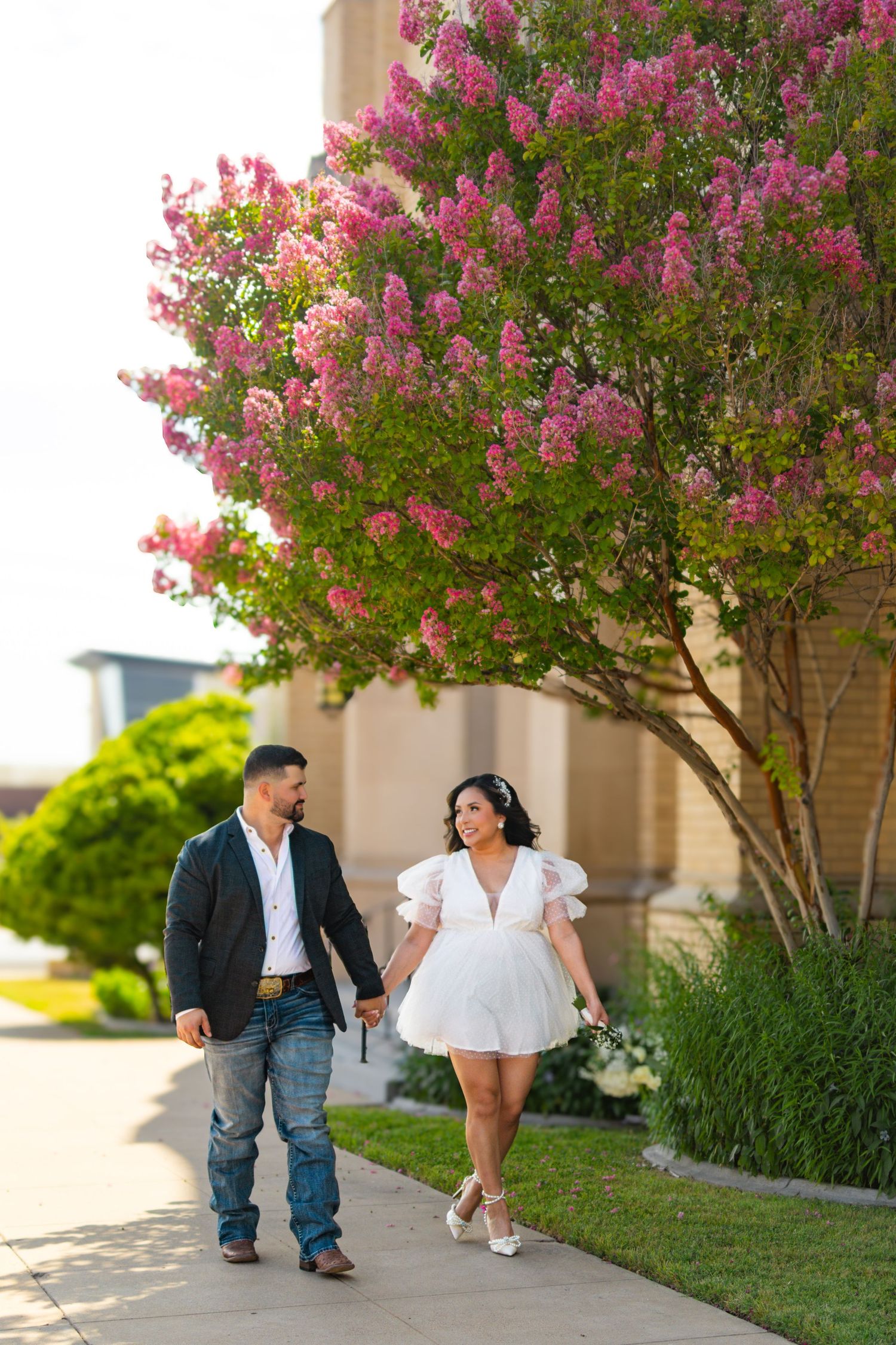 Couple walks hand in hand past blooming pink crape myrtle tree.