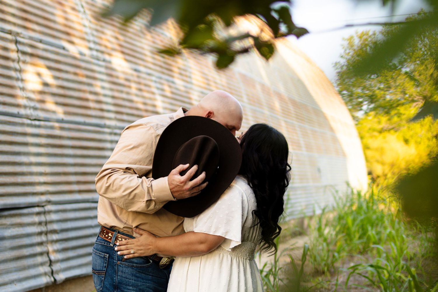 A romantic kiss captured against a rustic barn wall with soft lighting and natural scenery.