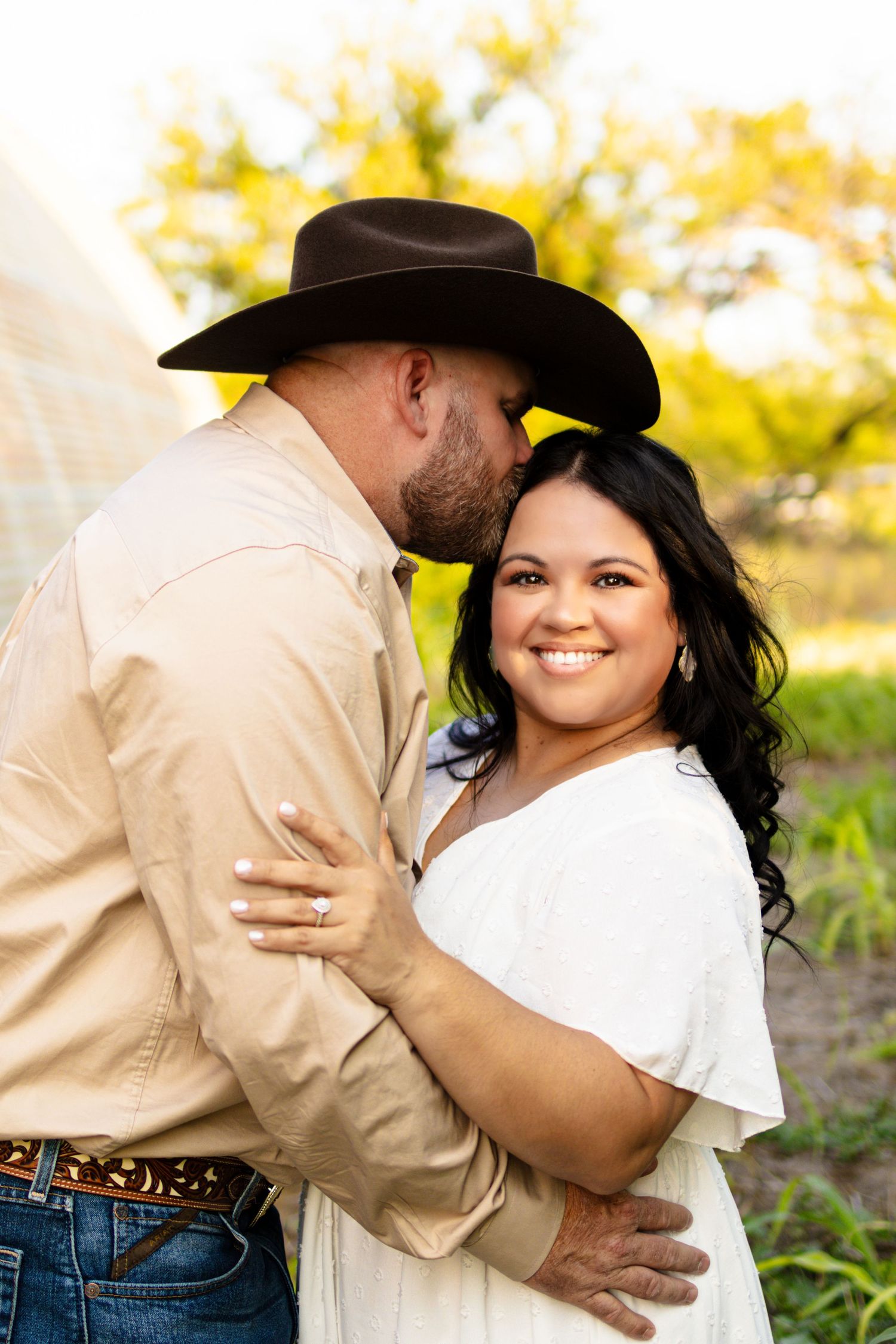 A romantic country-style engagement photo features a couple embracing outdoors with golden sunlight in the background.