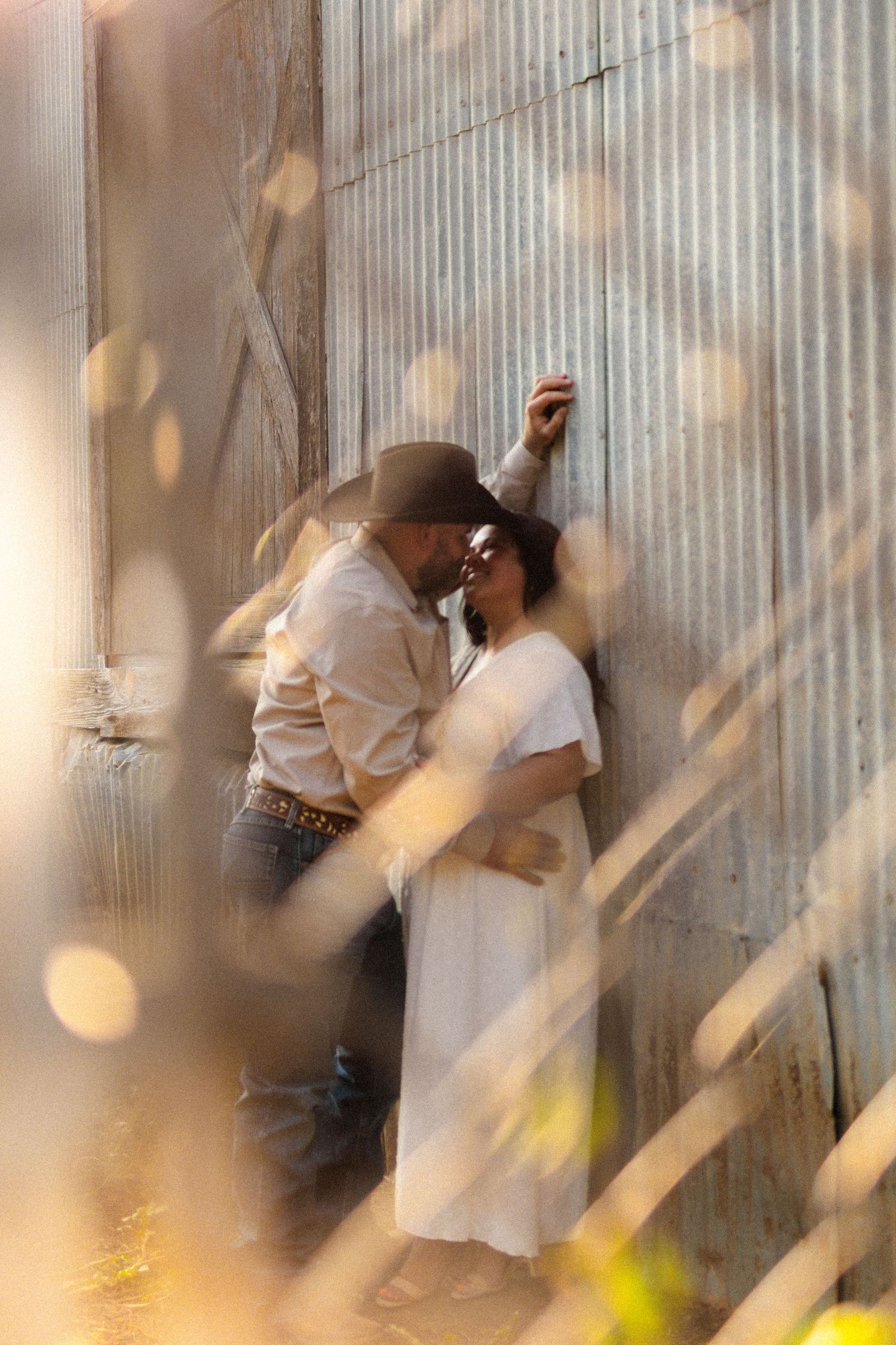 A dreamy engagement photo against a metal wall with soft bokeh effects and natural lighting.