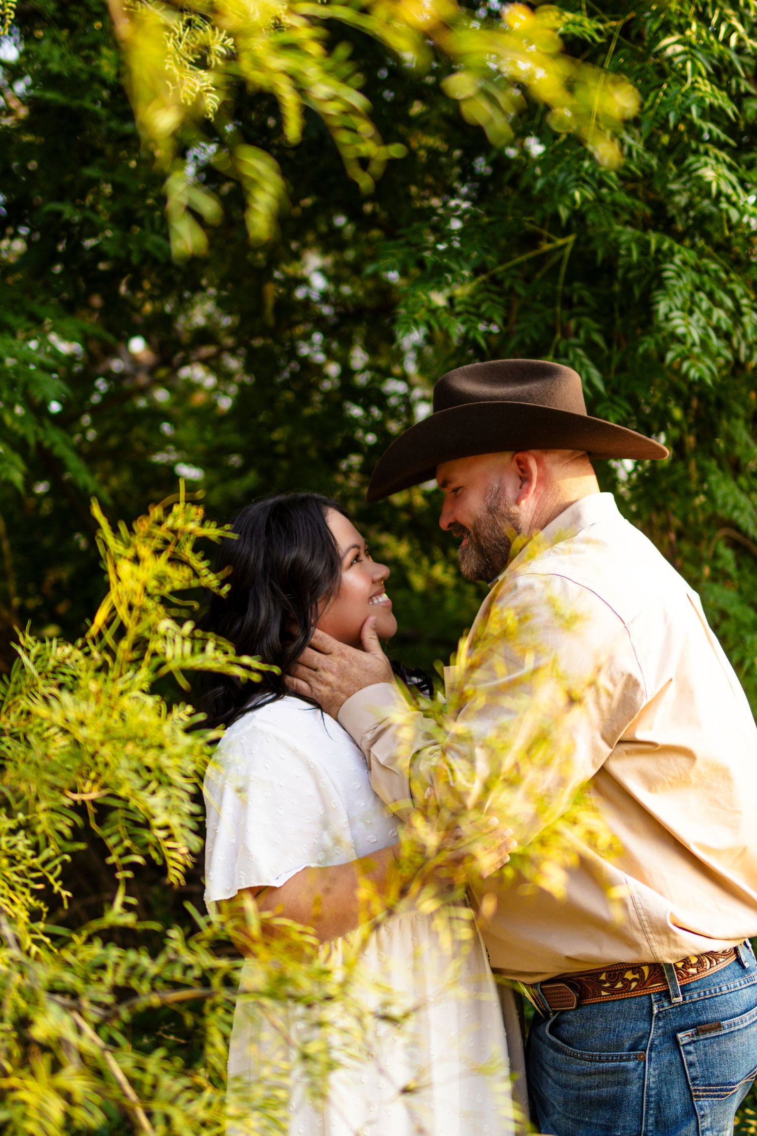 A couple shares an intimate moment in a garden setting with golden sunlight filtering through green foliage.