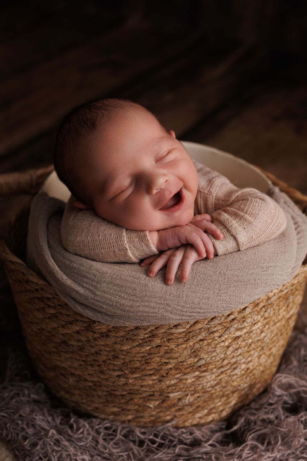 A sleeping newborn smiling while nestled in a cozy woven basket with beige fabric.
