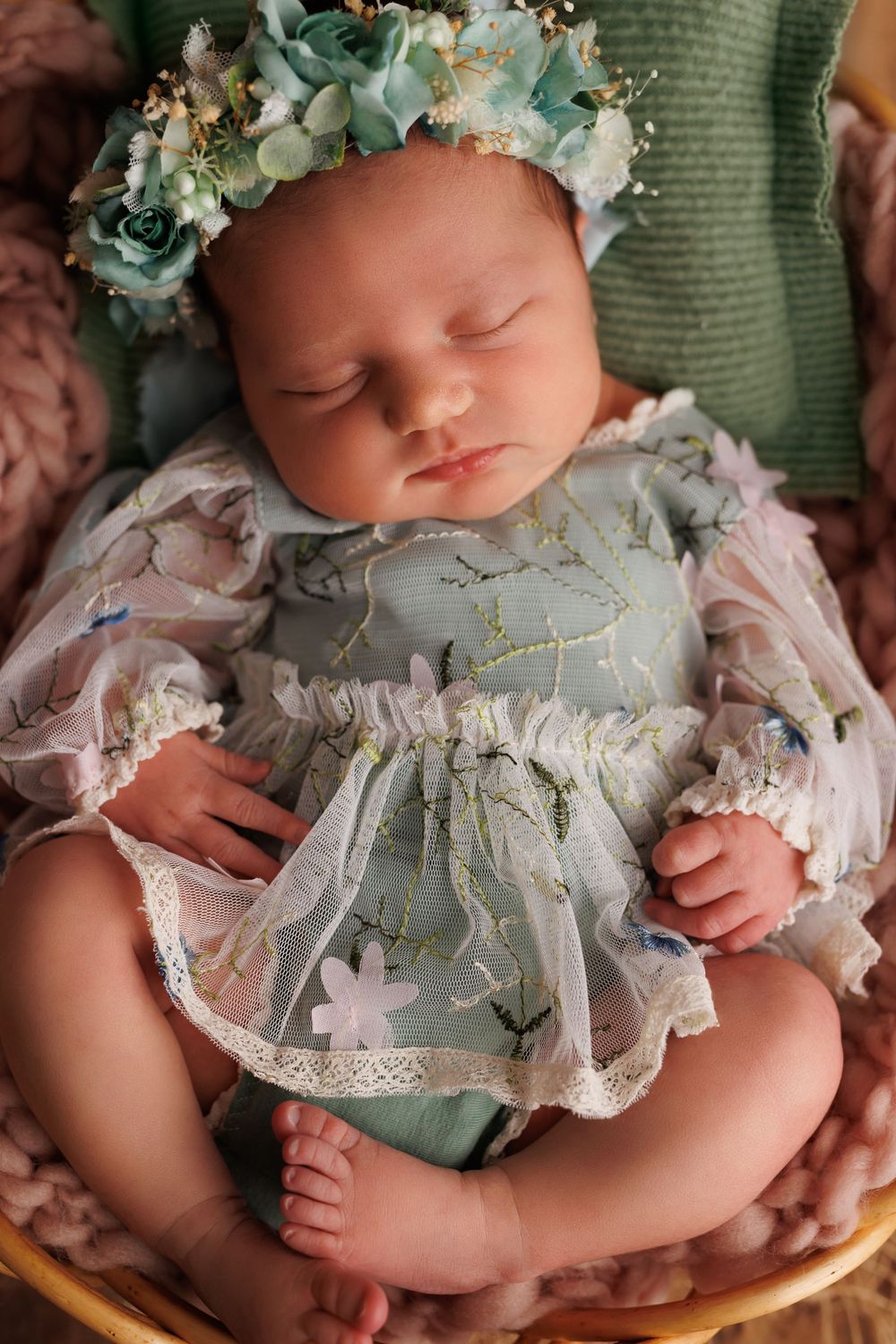 Sleeping infant wearing a delicate lace dress and floral crown made of soft blue eucalyptus and white blooms.