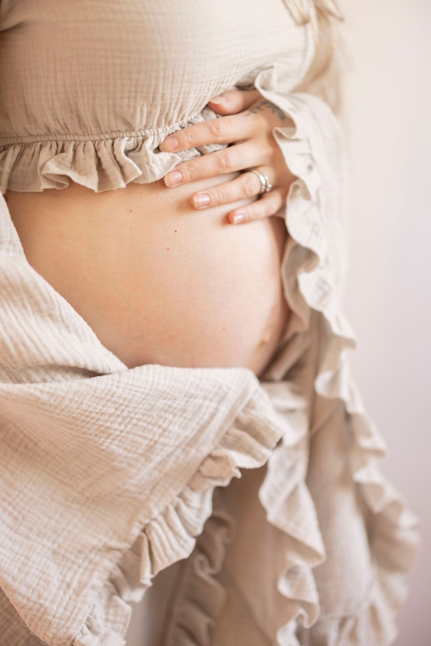 A delicate white ruffled maternity dress frames a pregnant belly with hands gently resting above.