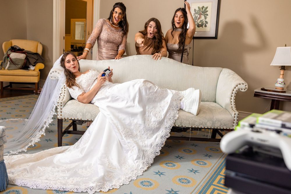 Bride and bridesmaids sharing a getting ready moment on a vintage sofa before the wedding ceremony.