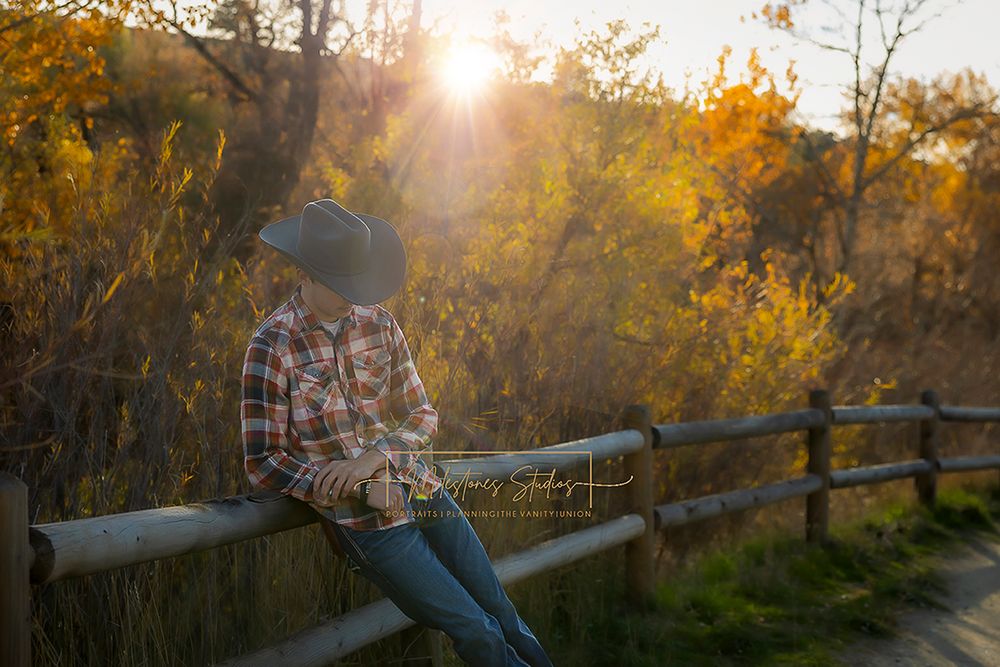 ©Milestones Portraits Boise Idaho senior photographer male wearing plaid, jeans, and a cowboy hat in the foothills backlit looking down