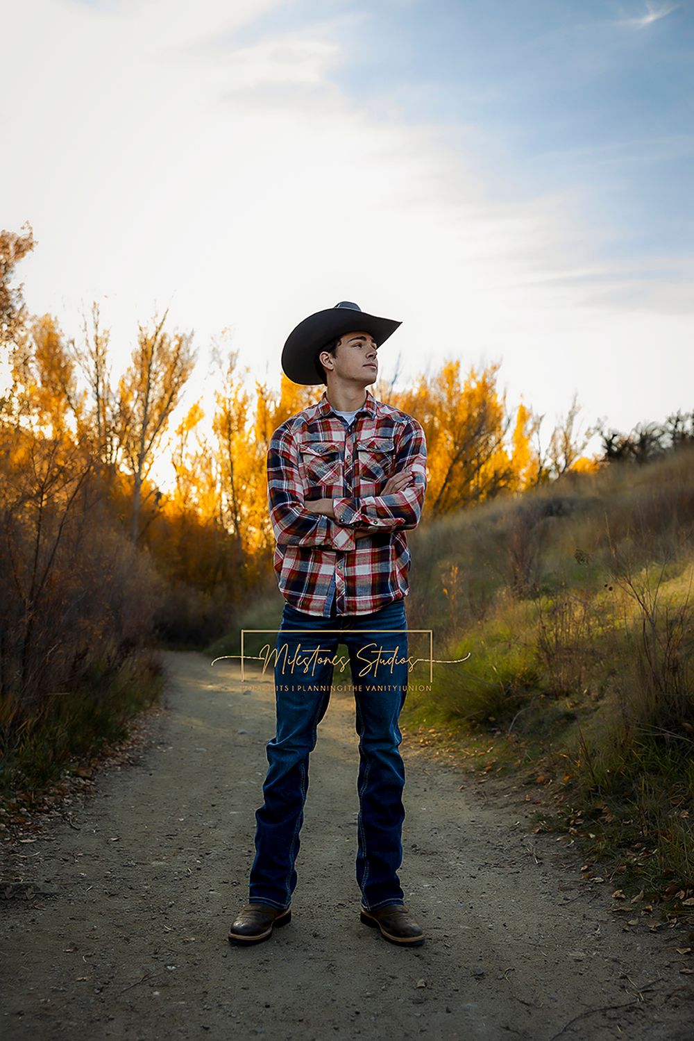 ©Milestones Portraits Boise Idaho senior photographer male wearing plaid, jeans, and a cowboy hat in the foothills