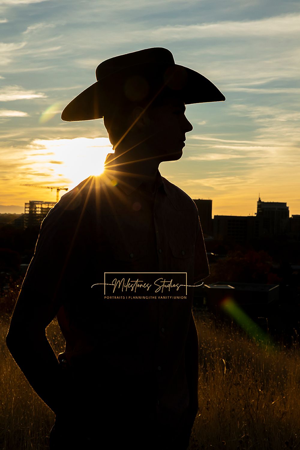 ©Milestones Portraits Boise Idaho senior photographer male wearing plaid, jeans, and a cowboy hat in the foothills silhouette form