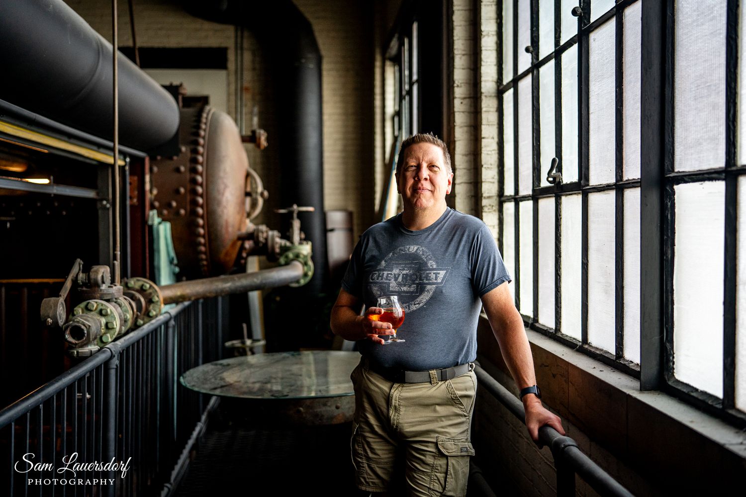 Photographer holding a camera photographs through floor-to-ceiling windows in a rustic industrial interior space.