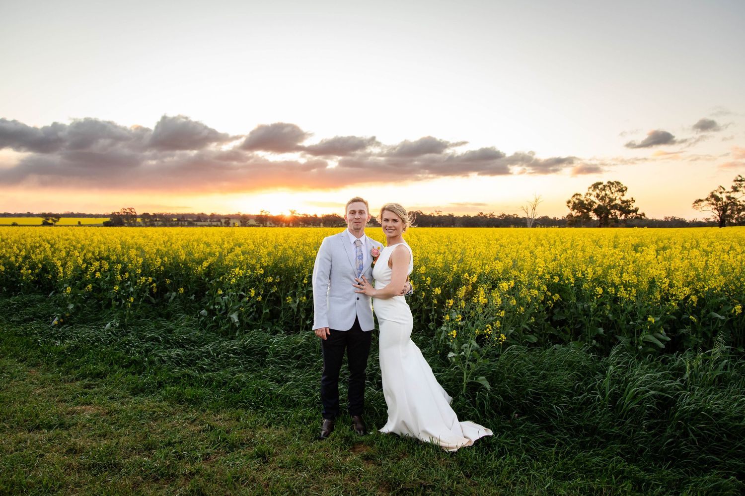 Couple stands together at sunset in a vibrant yellow canola field during golden hour.