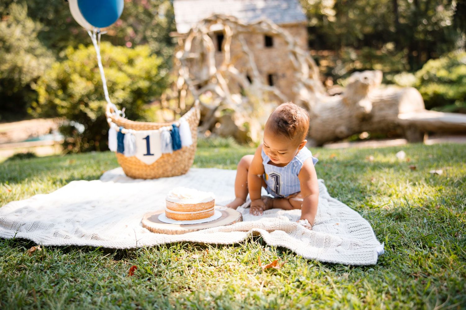 A child lies on a white blanket in a sunny garden while drawing or coloring on paper.