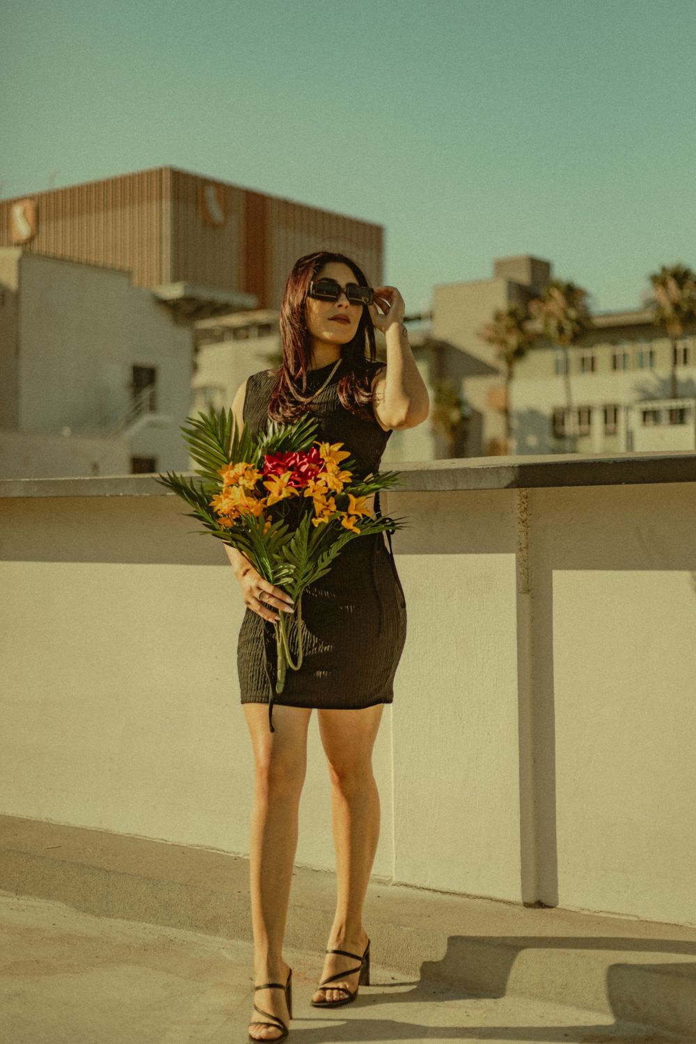 Model in a black dress poses with a vibrant bouquet of flowers on an urban rooftop at golden hour for Portrait photography