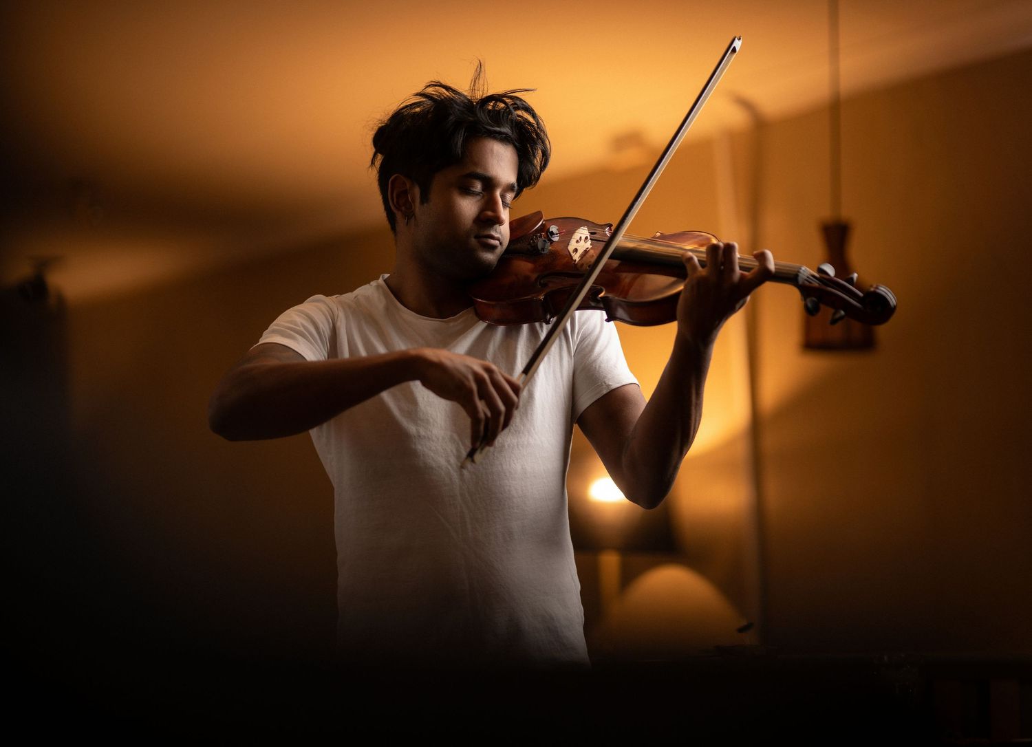 Musician playing violin in warm dramatic amber lighting, creative musician portrait photography Southampton