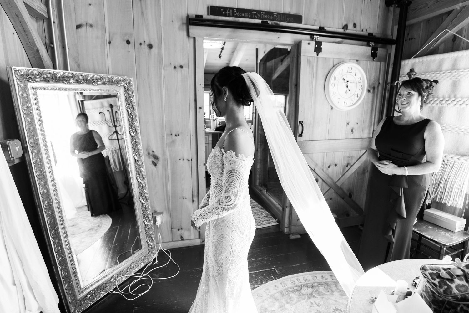 Black and white photo of bride in lace gown viewing reflection in ornate mirror.