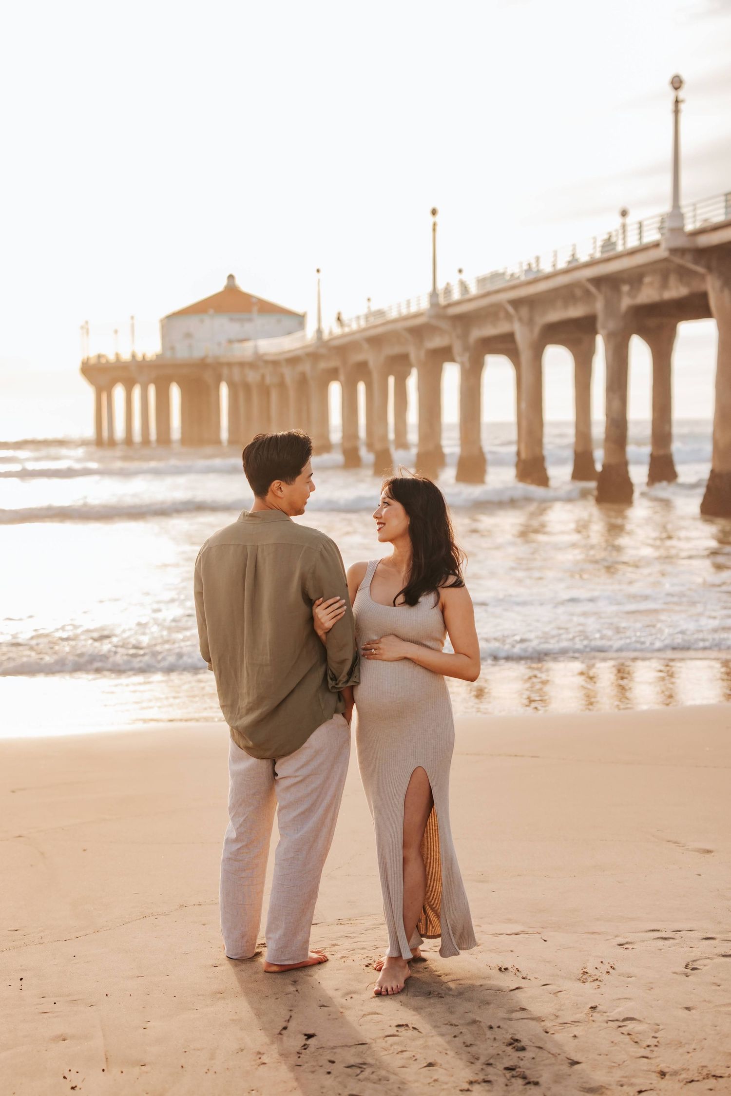 A couple shares a romantic moment at sunset on the beach by a picturesque pier at Manhattan Beach.
