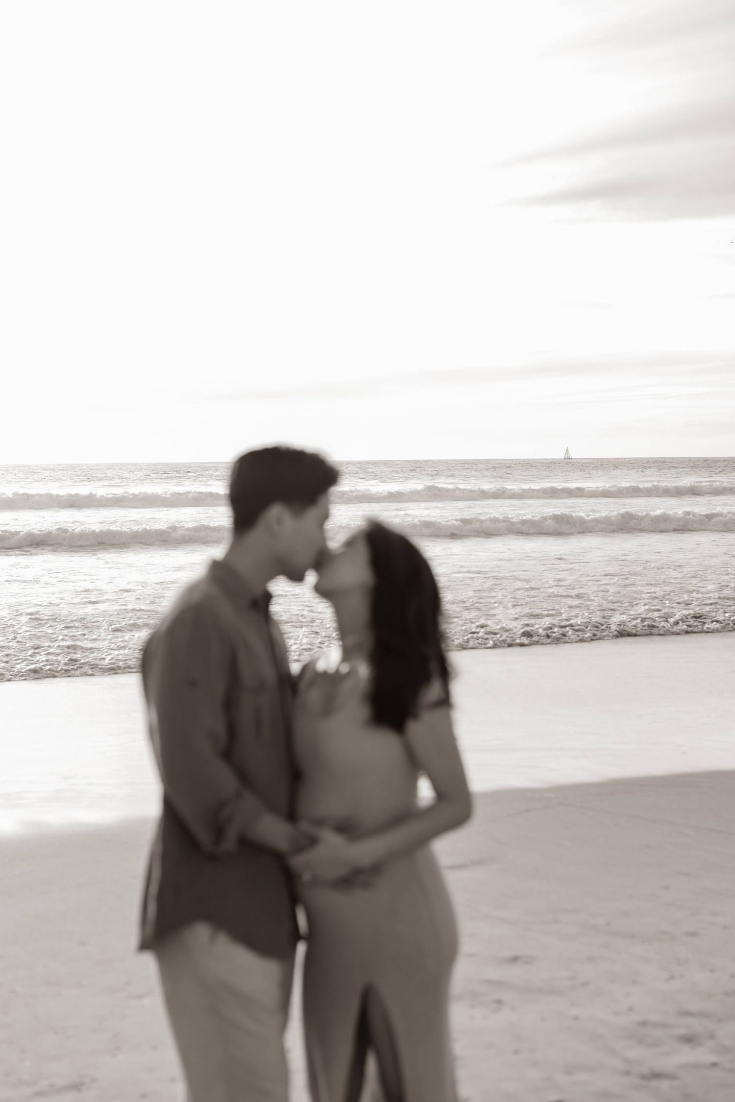 A romantic couple sharing an intimate moment on a peaceful beach with ocean waves in the background.