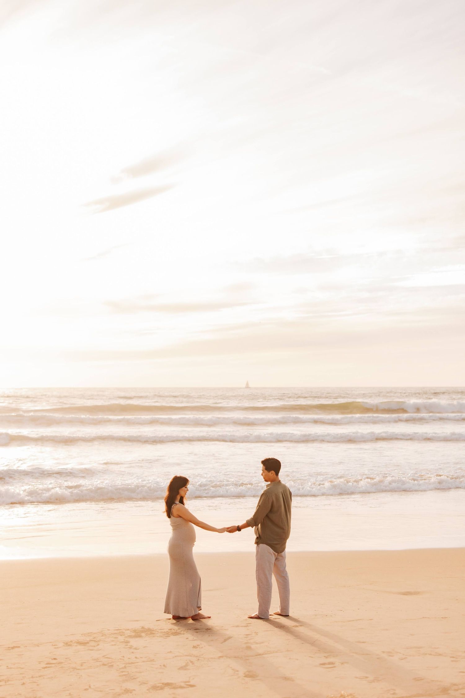 Two people holding hands on a serene beach at sunset with gentle waves rolling in along the shoreline.