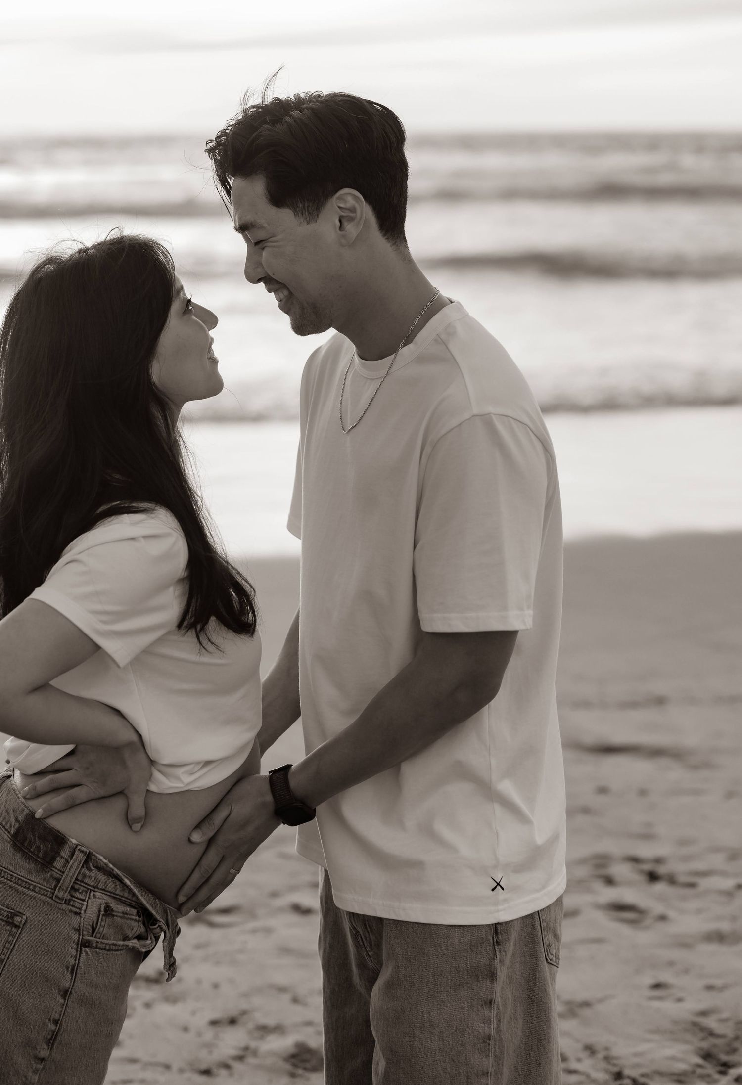 A romantic black and white photo of a couple sharing a lighthearted moment together on the beach.
