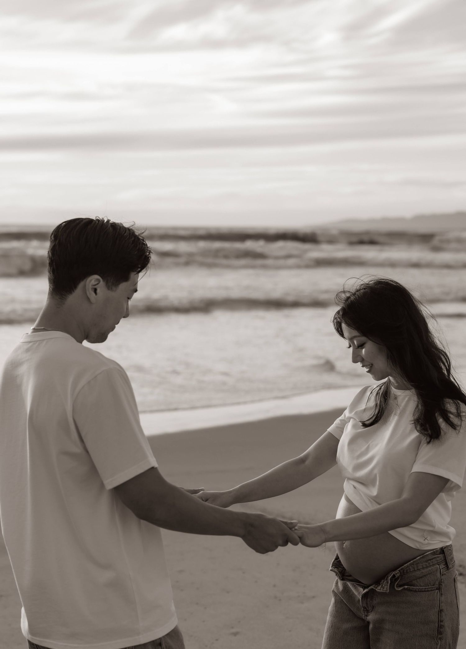 Romantic black and white photo of a couple holding hands on a misty beach with ocean waves in the background.
