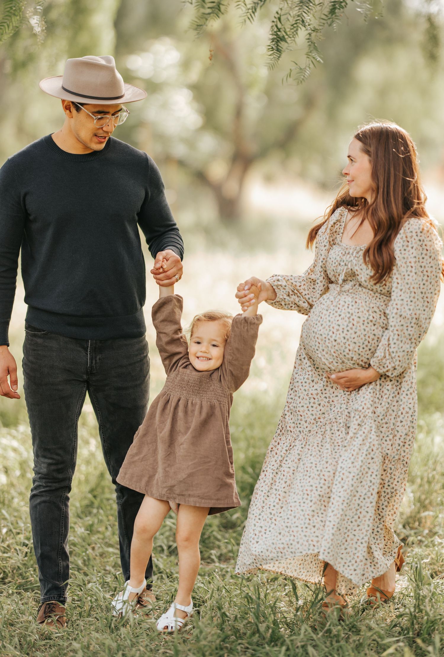 Family enjoying outdoor moment as toddler in brown dress plays between parents in garden setting.