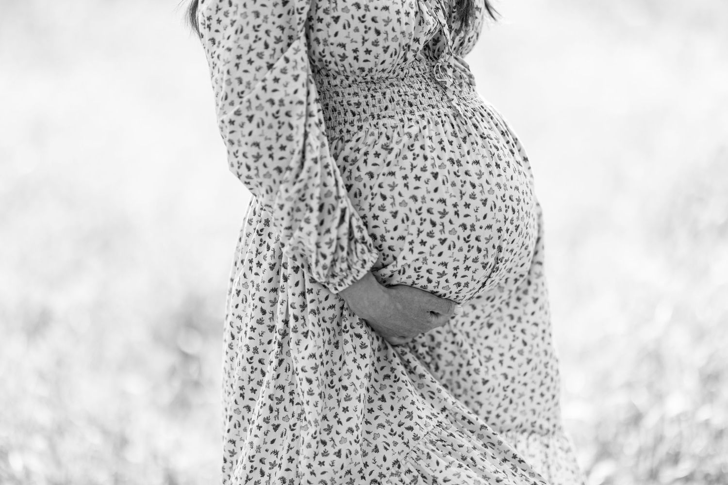 Black and white portrait highlighting flowing maternity dress in field.
