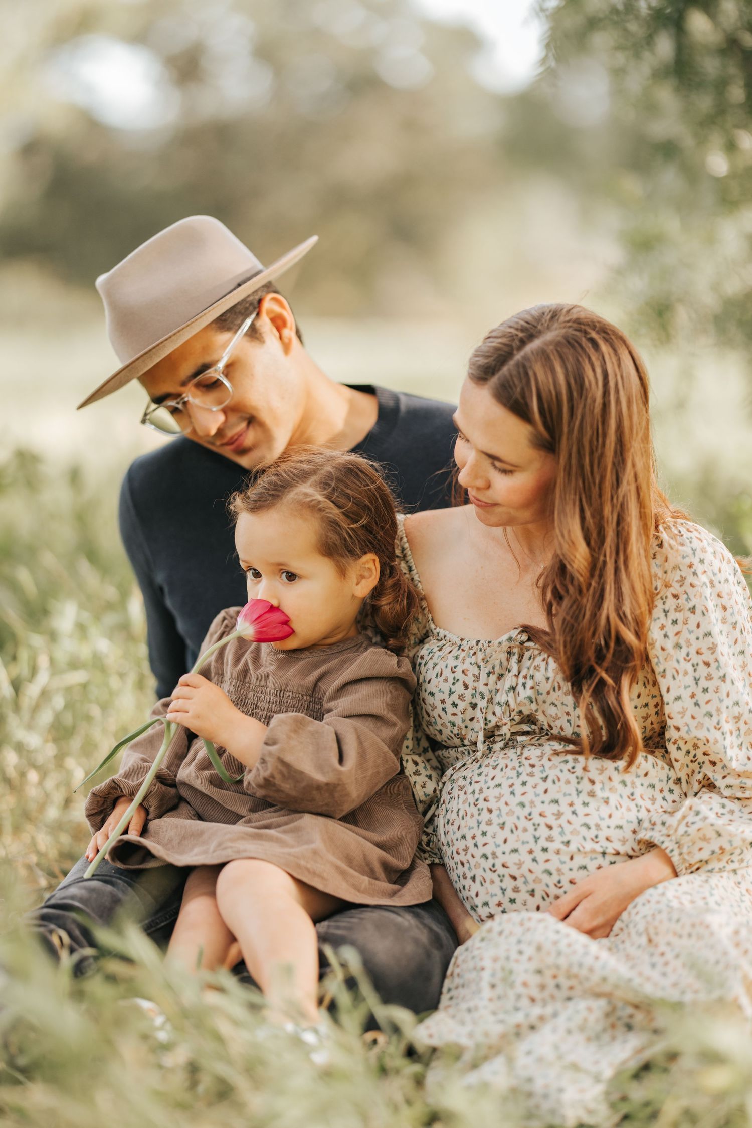 Family sits together in tall grass during golden hour photo session.