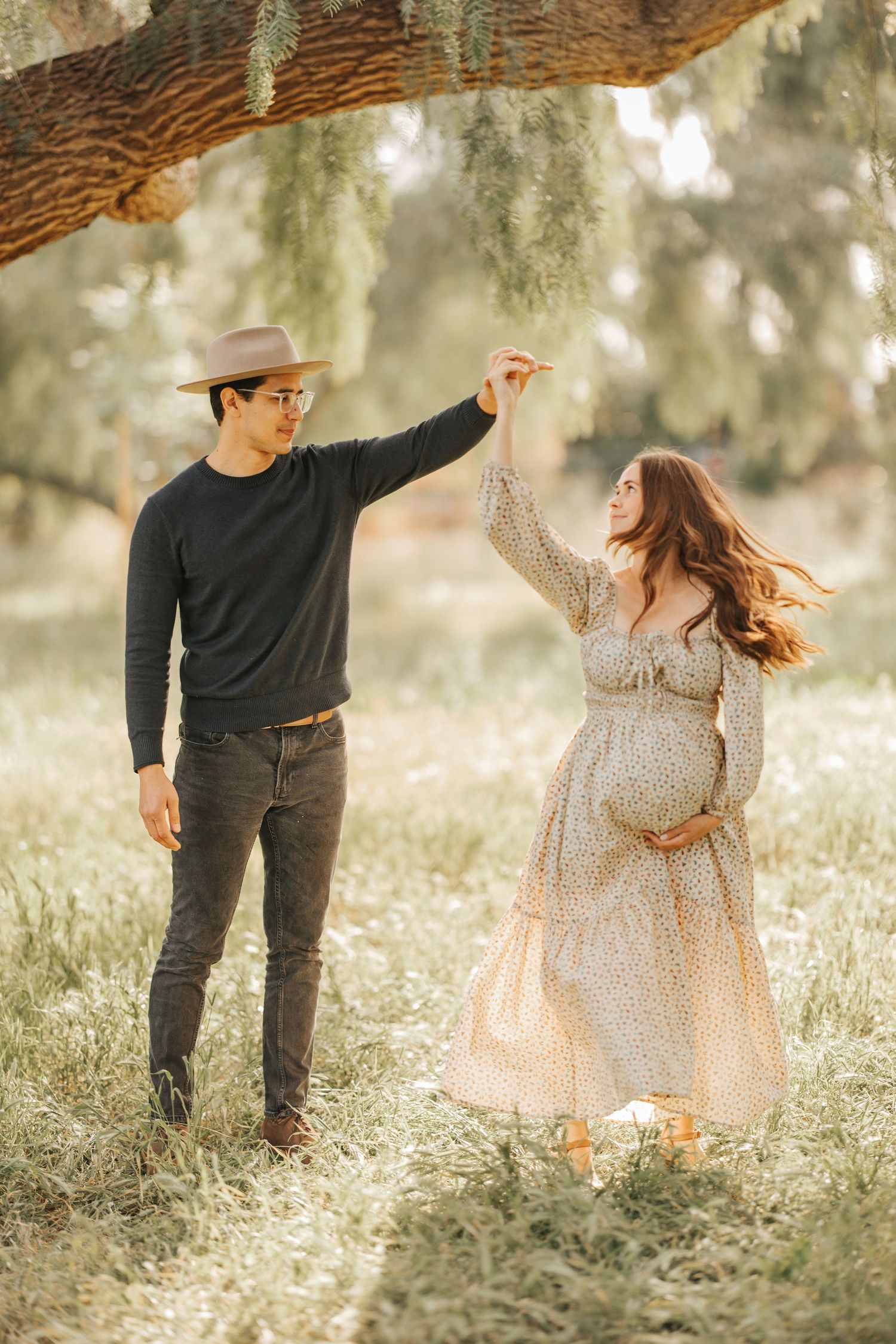 Dancing couple in a dreamy outdoor setting with flowing dress and hat.