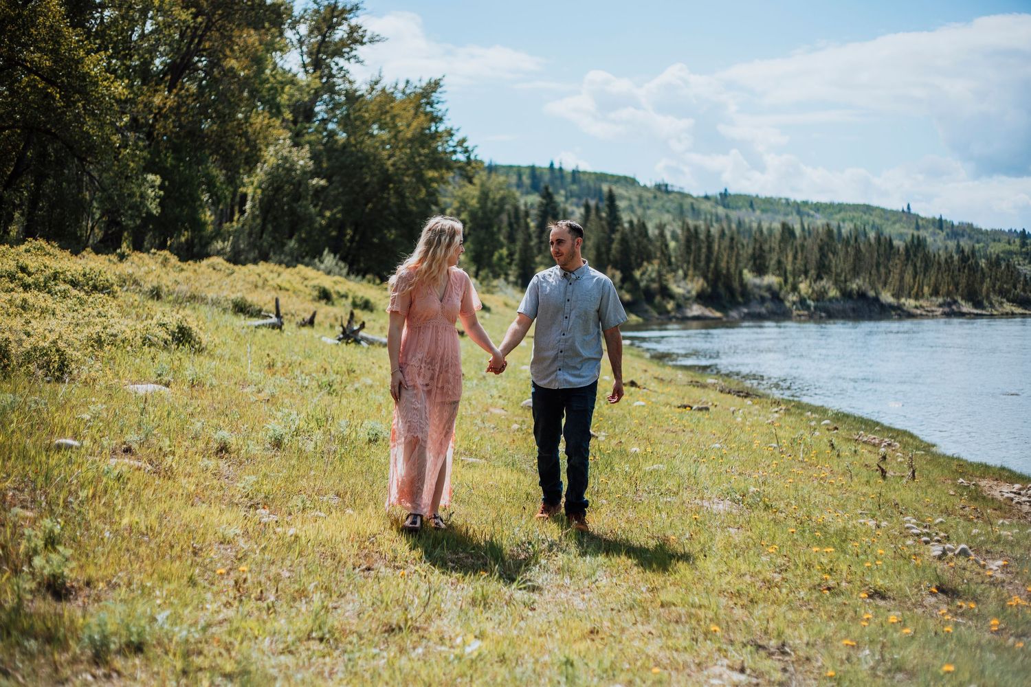 Couple holding hands while walking along scenic lakeside meadow.