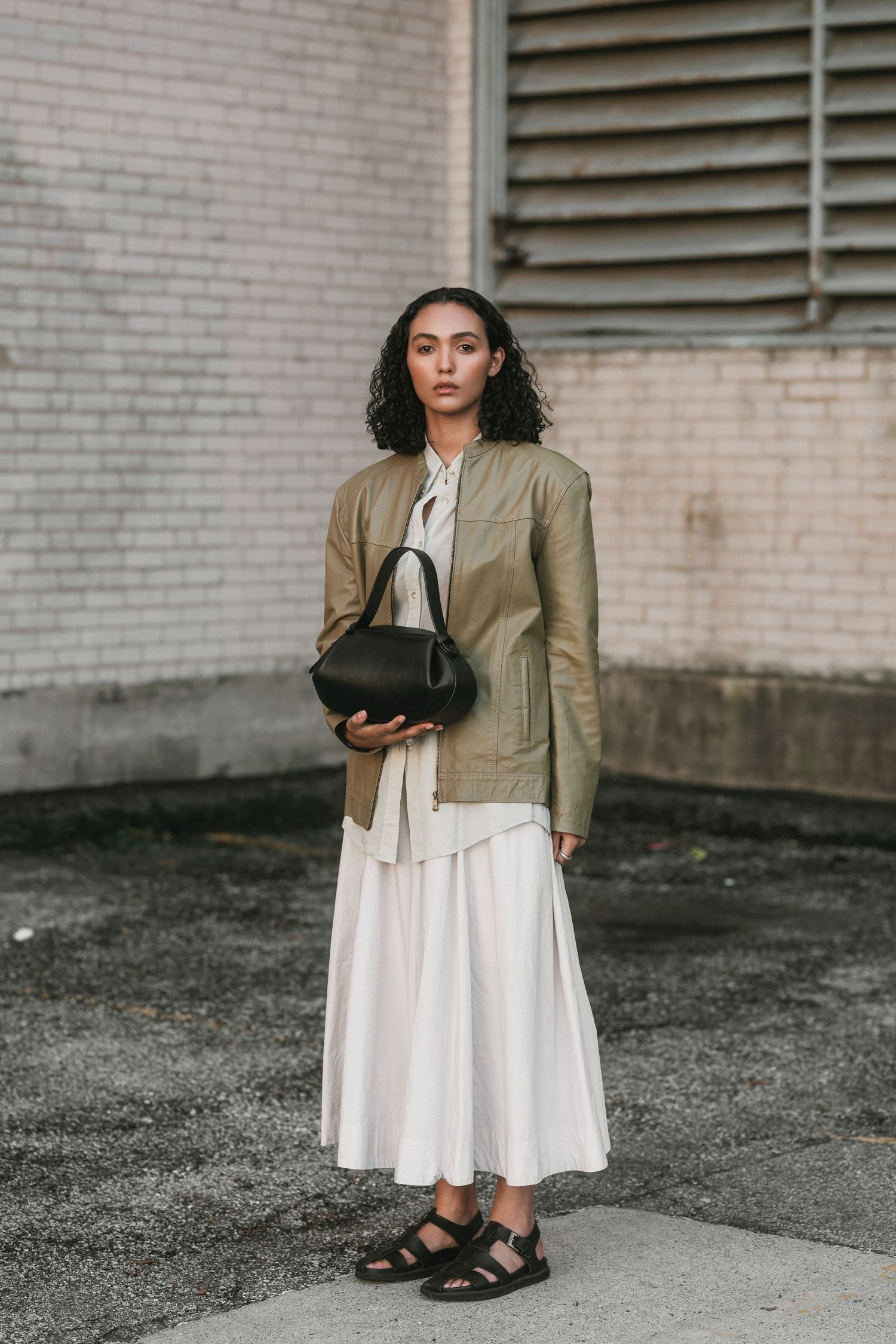 Young woman with wearing a green jacket, standing against a white brick backdrop in Downtown Cincinnati