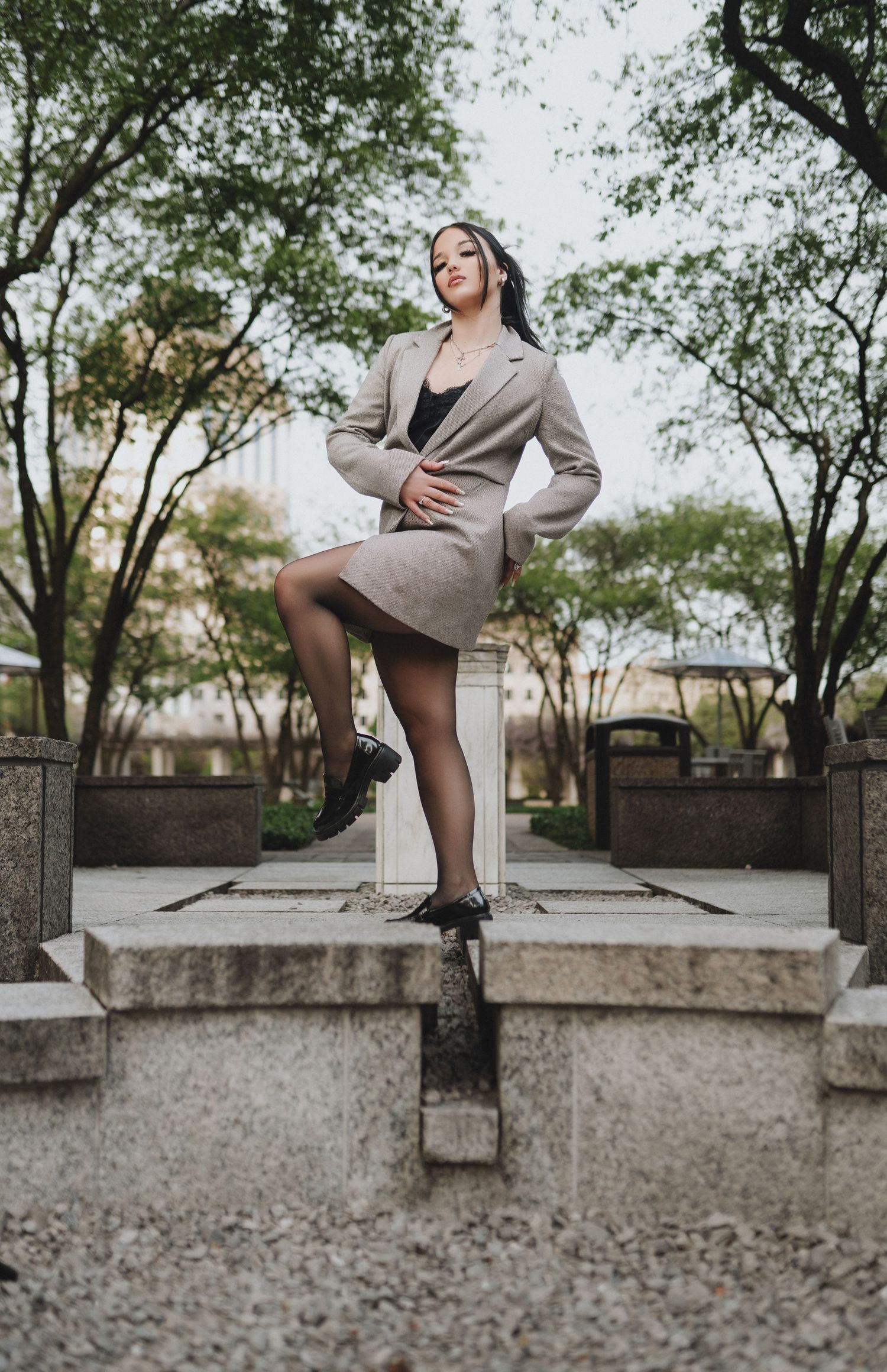 Woman in beige blazer skirt suit and black tights posing on stone steps in park setting in Cincinnati