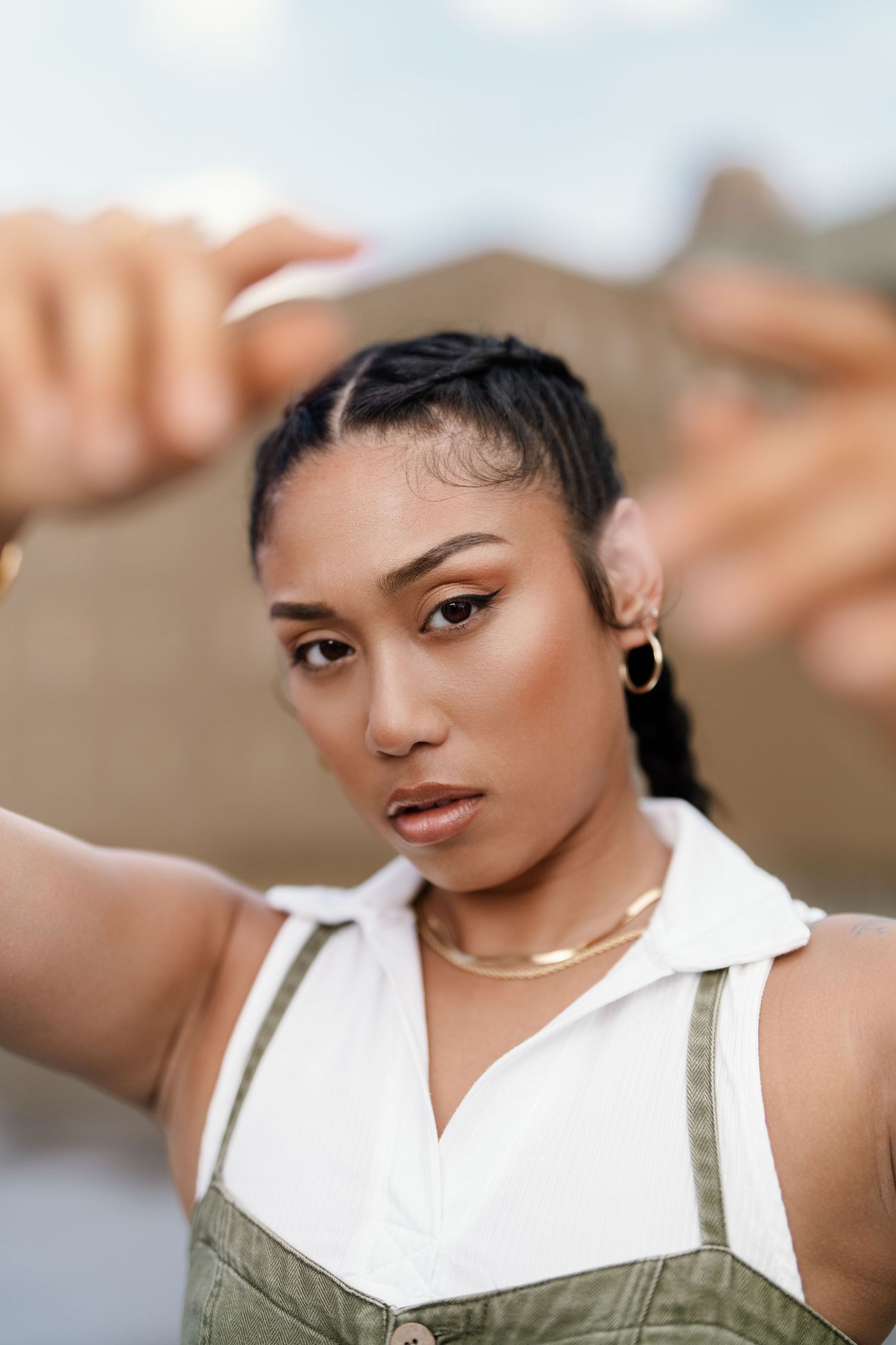 Young woman in green overalls and white top reaching toward camera with gold jewelry outdoors in Cincinnati