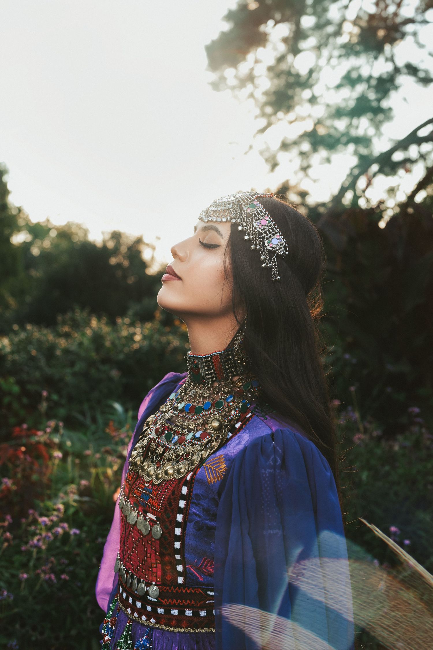 Woman in traditional Afghan embroidered clothing and silver headpiece standing in a sunlit garden in Cincinnati